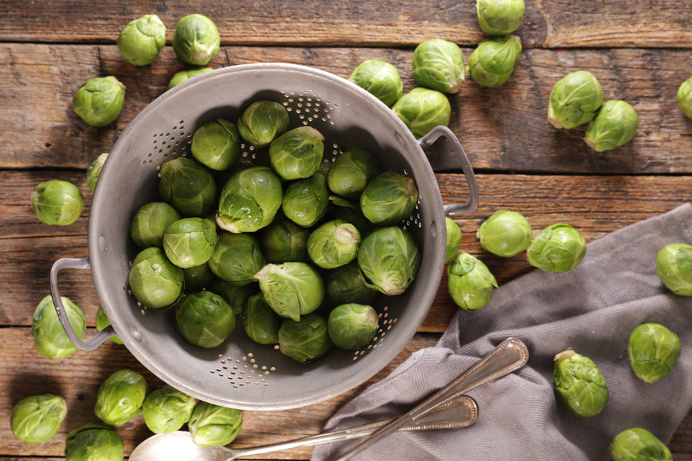brussels sprouts in a metal colander and on a wooden table with a fabric napkin and cutlery
